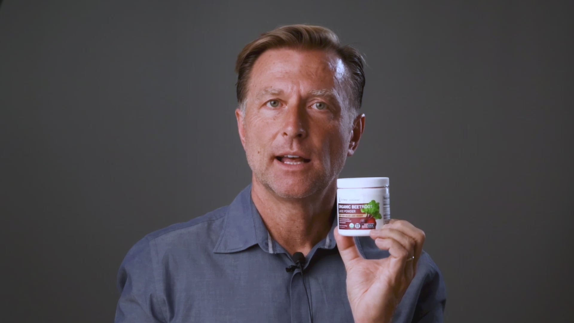 Dr Berg holds a jar of Dr Berg Organic Beetroot Juice Powder – Raw, Fresh, USDA Organic for circulation and wellness benefits.