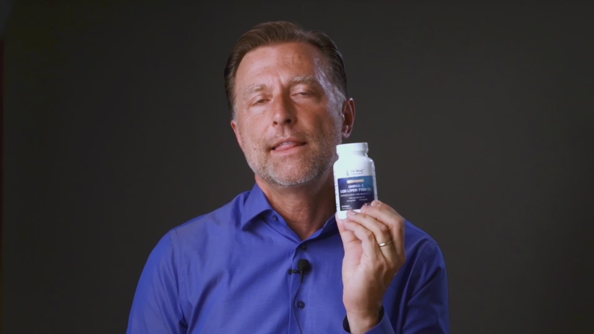 Person holding Dr Berg Wild-Caught Omega-3 Cod Liver Fish Oil DHA EPA – 60 Softgels bottle, promoting heart and brain health supplements.